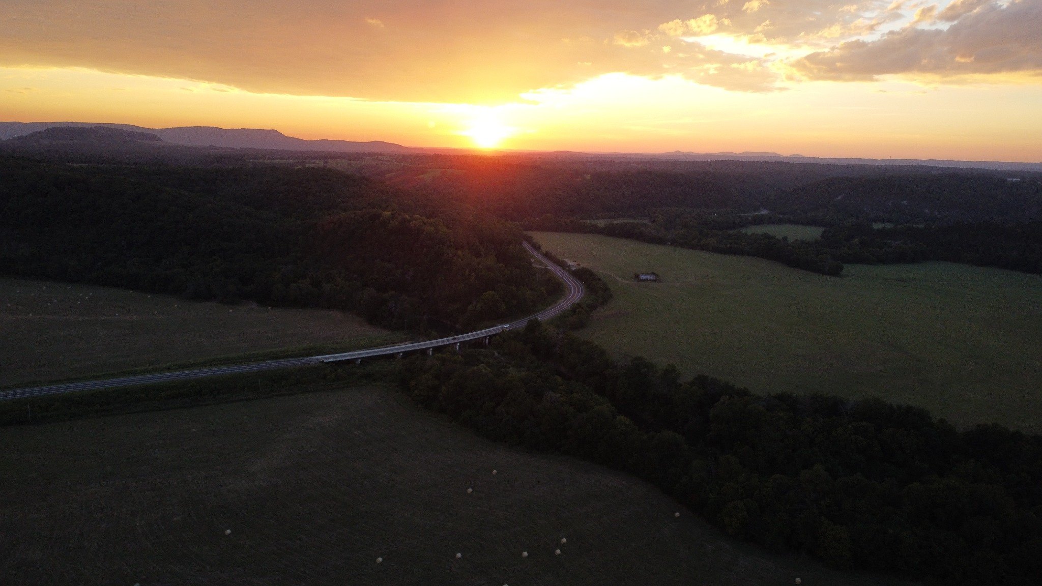 Aerial sunset across fields and wooded ridges